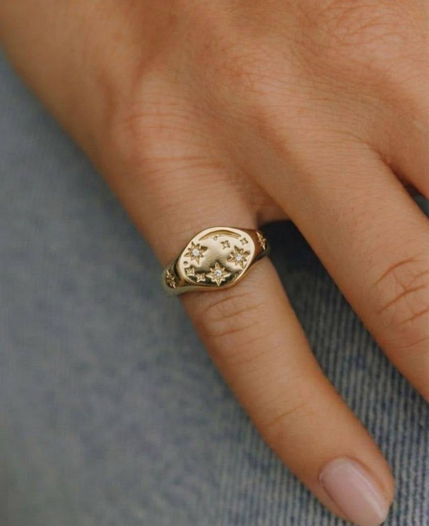 Gold ring with star design on a finger against a denim background